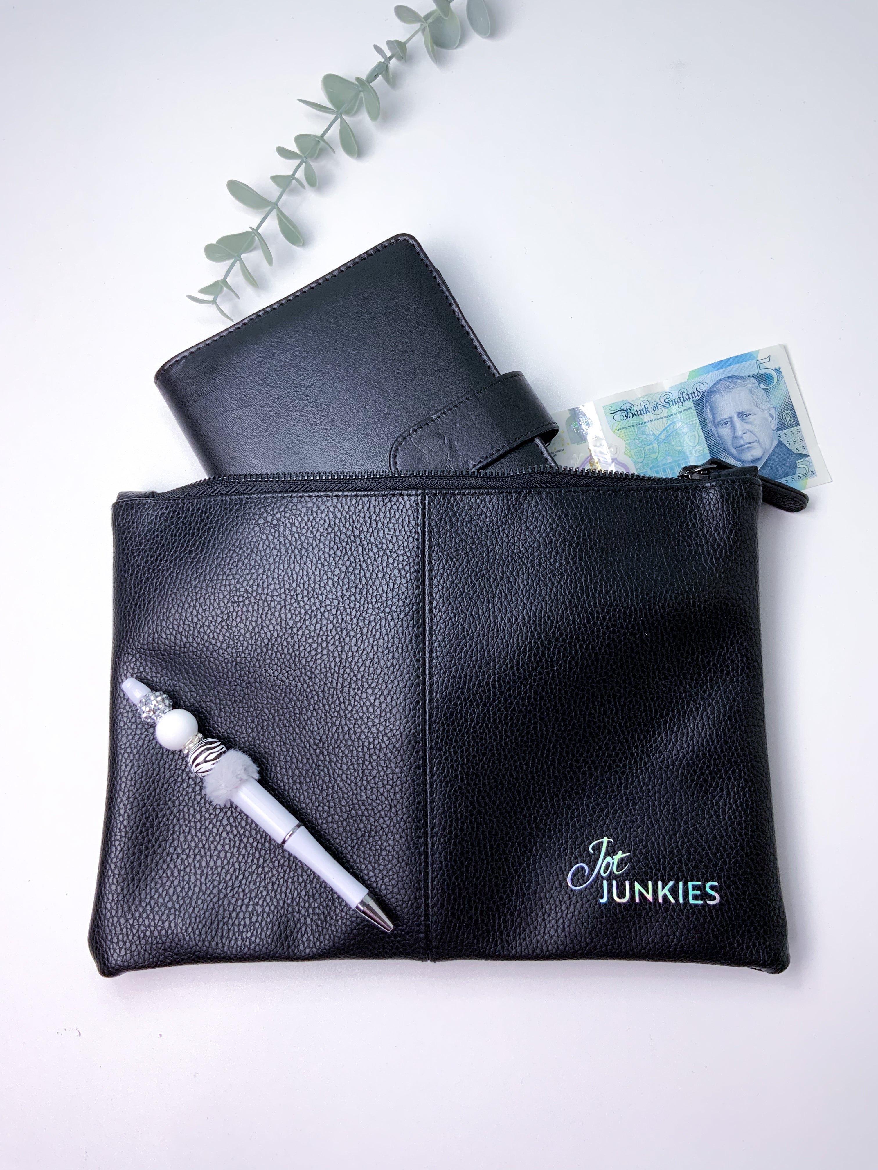 Black leather pouch with a pen and money on a white background, featuring 'Jot Junkies' branding.