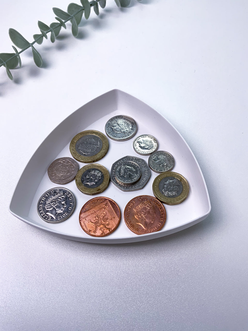Collection of coins on a white triangular dish with a light gray background