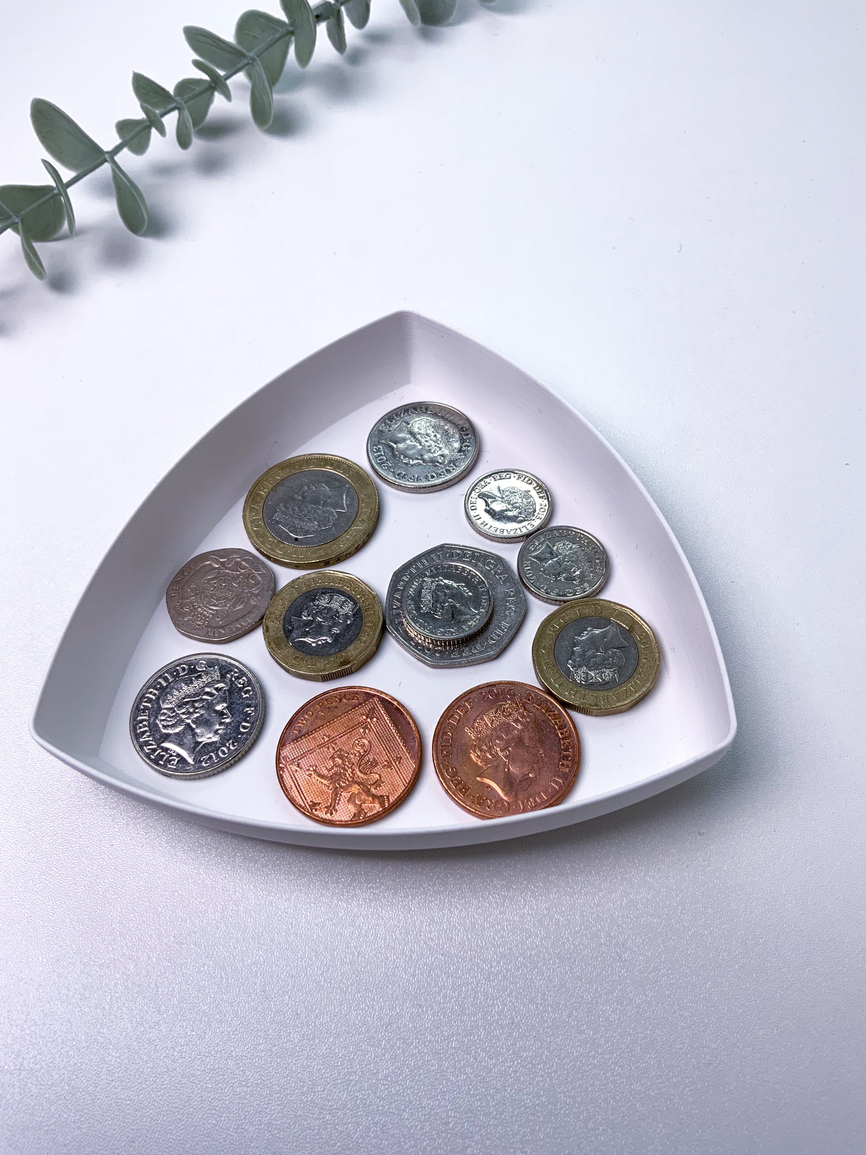 Collection of coins on a white triangular dish with a light gray background